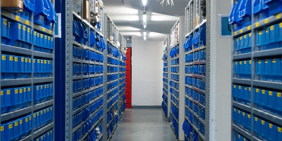 Pasillo de almacén industrial con estanterías altas y cajas azules.
