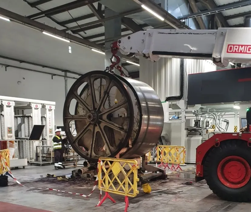 Grua industrial moviendo una enorme rueda metálica dentro de una nave