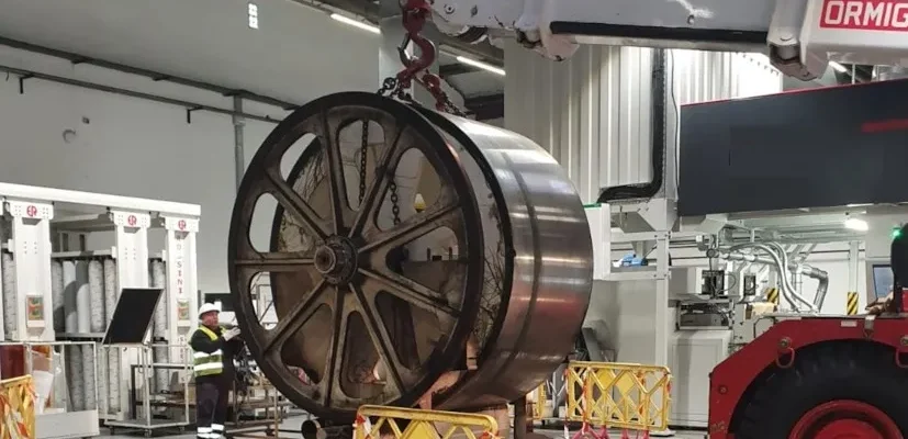 Grua industrial moviendo una enorme rueda metálica dentro de una nave