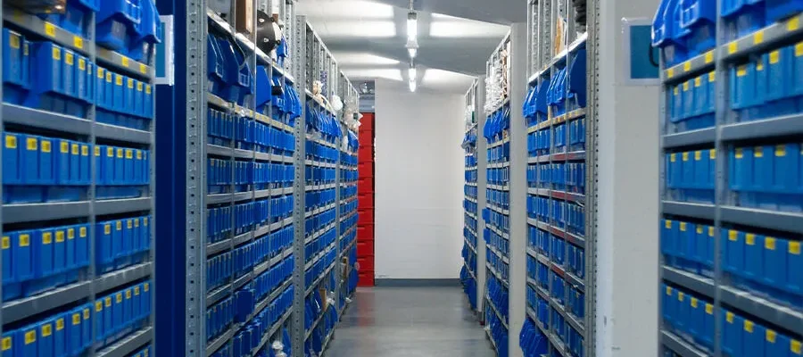 Pasillo de almacén industrial con estanterías altas y cajas azules.